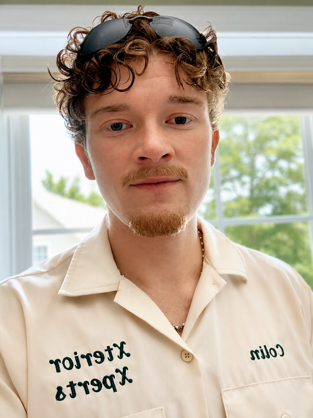 Young man with curly brown hair and a goatee wearing a cream-colored embroidered shirt.
